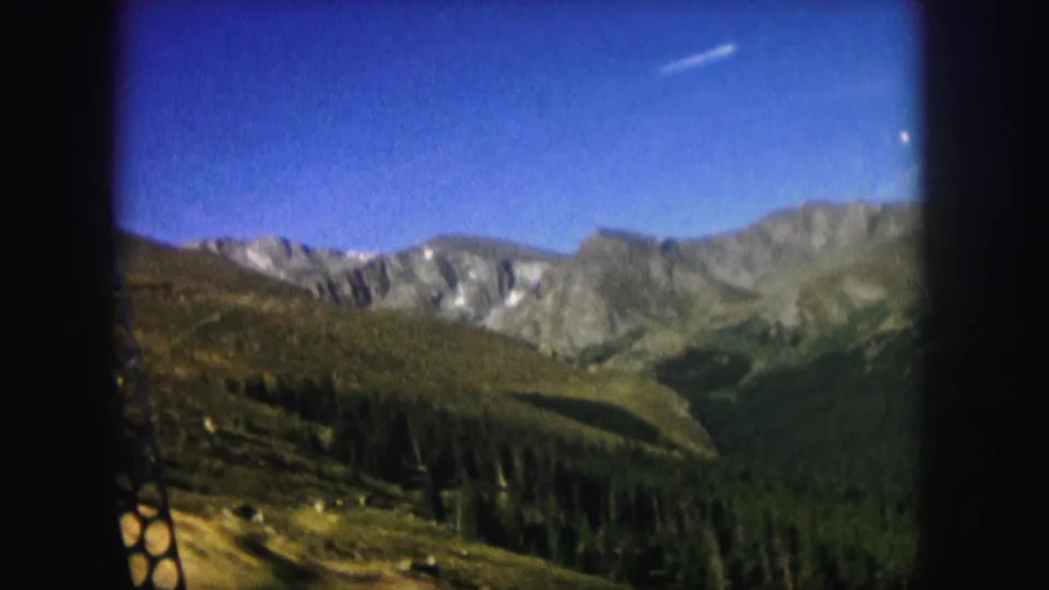Scenic 1958 Colorado mountain view with a forested valley below rocky ridges and green slopes, filmed on 8mm home-movie stock.