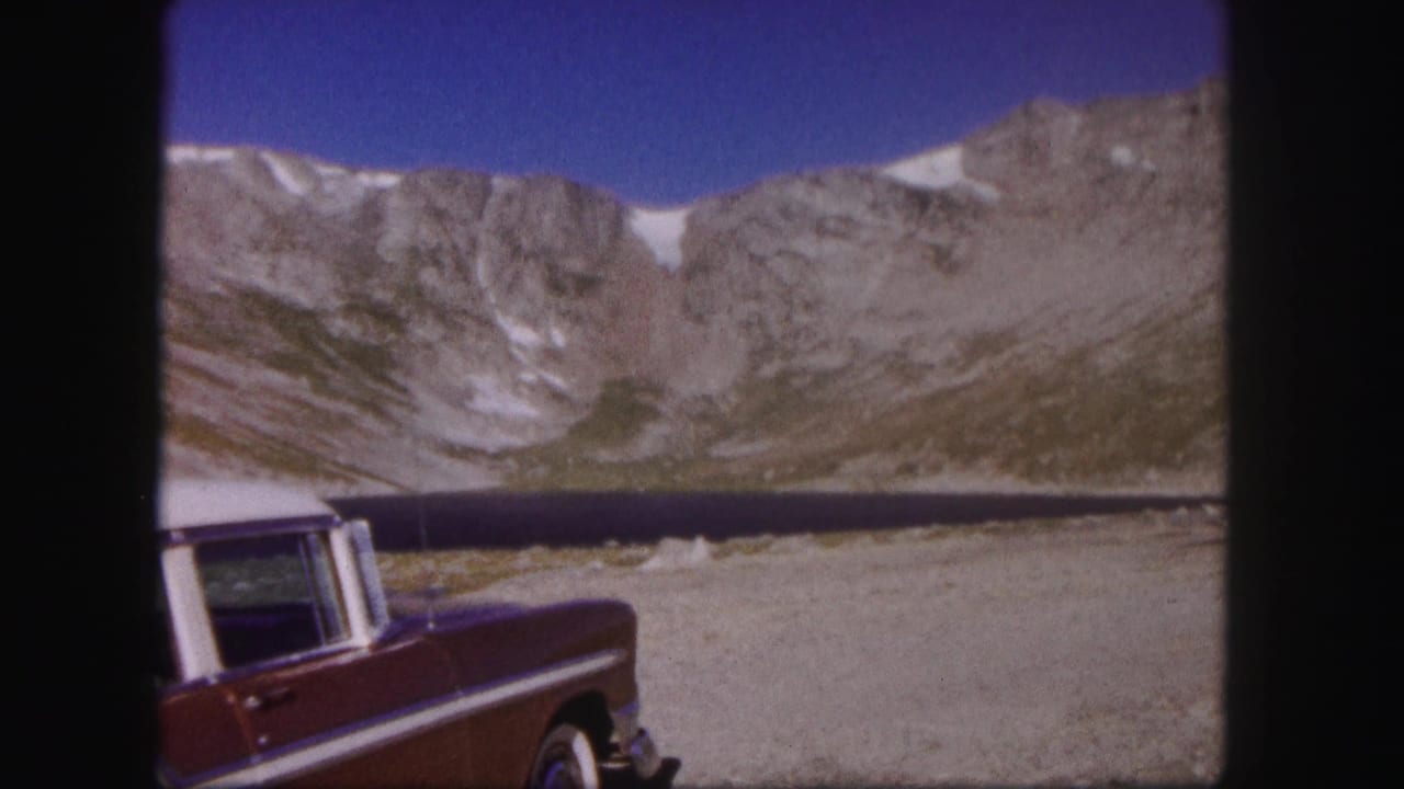 1958 Colorado 8mm frame showing a maroon older car near an alpine lake below rocky, snow-dusted mountains.