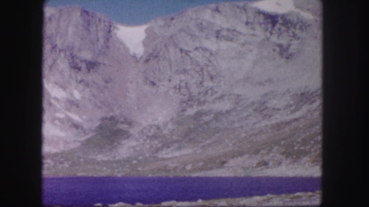 Rocky mountain slope with snow patches rising above a deep blue lake.