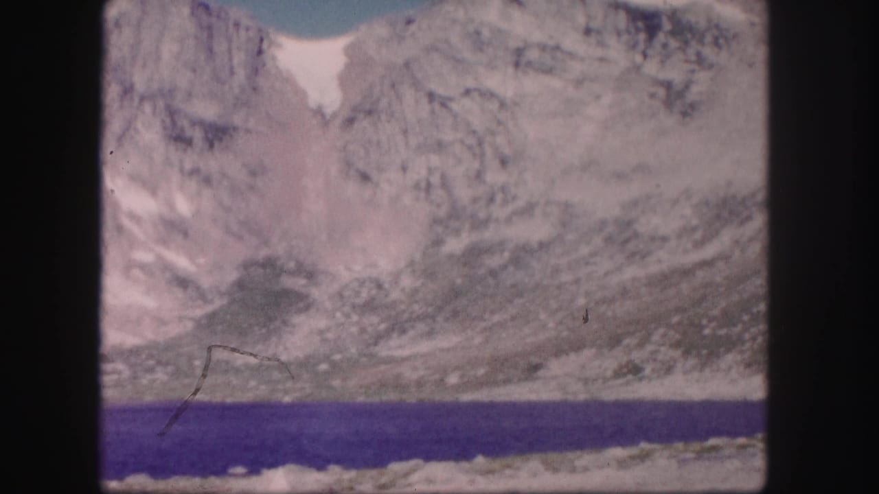 Rocky mountain basin and dark lake water with a small bird or speck crossing the frame.