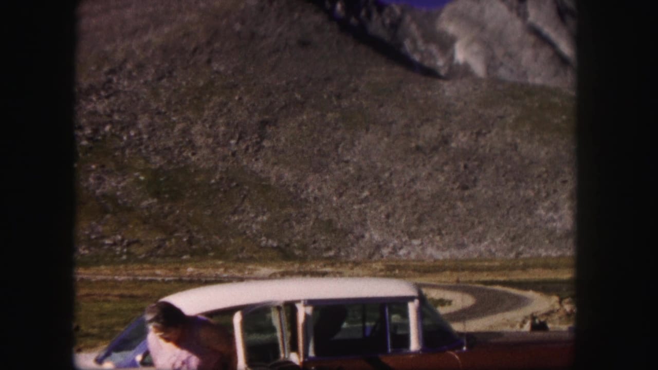 Two-tone station wagon parked on a mountain road with a woman partly visible beside it.