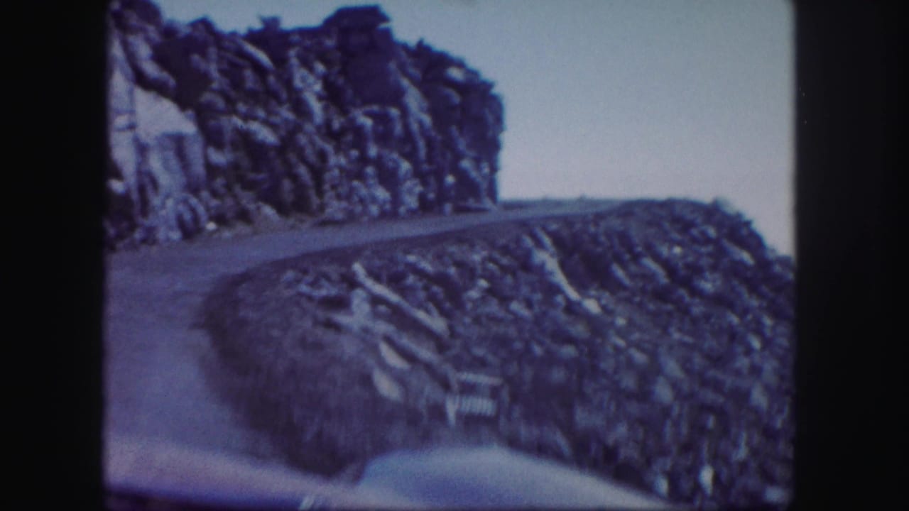 Narrow mountain road curves along a rocky cliff with open sky beyond.