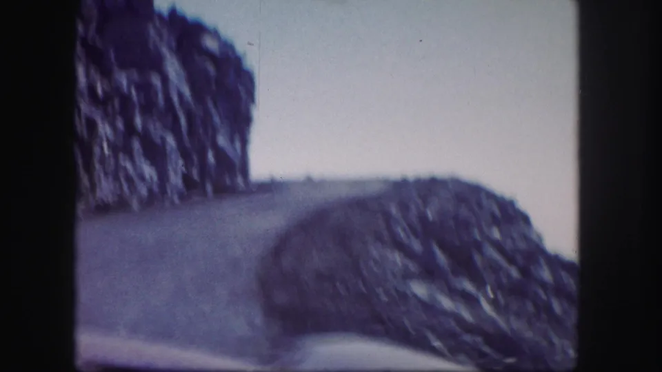 1958 Colorado 8mm frame showing a soft, grainy view of a road rounding a rocky bend in high mountain terrain.