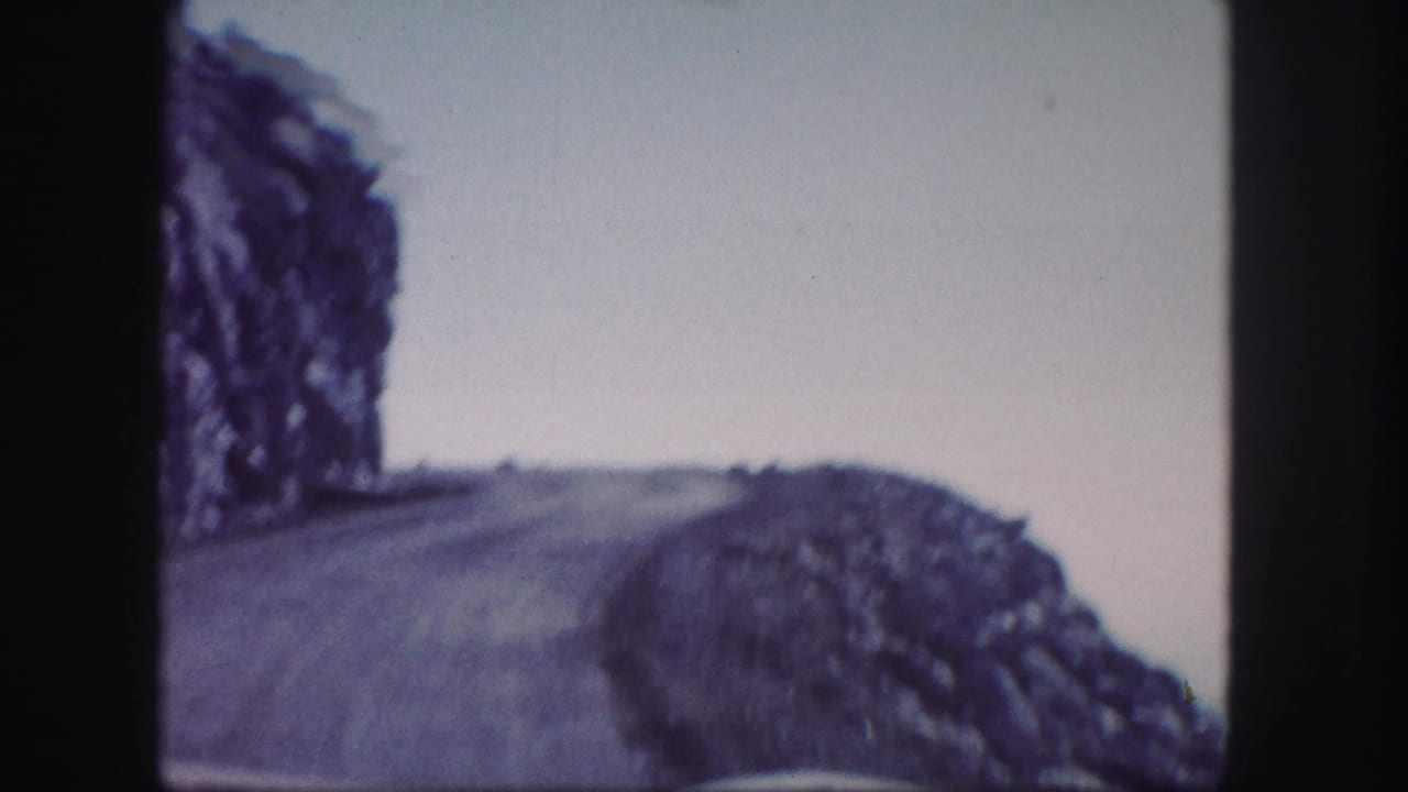 Winding mountain road beside rocky slopes under a pale sky.