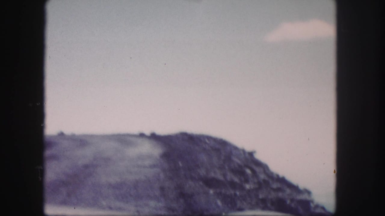 1958 Colorado 8mm frame with a rocky ridge rising beneath a muted, cloudy sky.