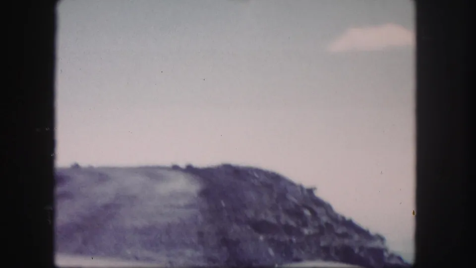 1958 Colorado 8mm frame with a rocky ridge rising beneath a muted, cloudy sky.