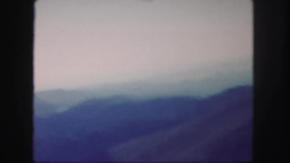 1958 Colorado 8mm frame showing blue-purple mountain layers fading into mist under overcast conditions.