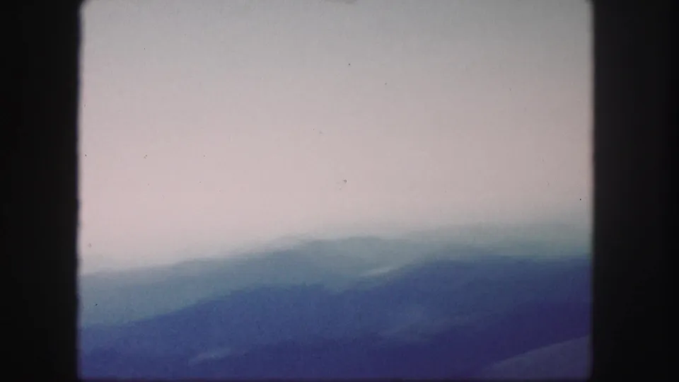 1958 Colorado 8mm frame with distant mountain ranges softened by atmospheric haze and a cloudy sky.