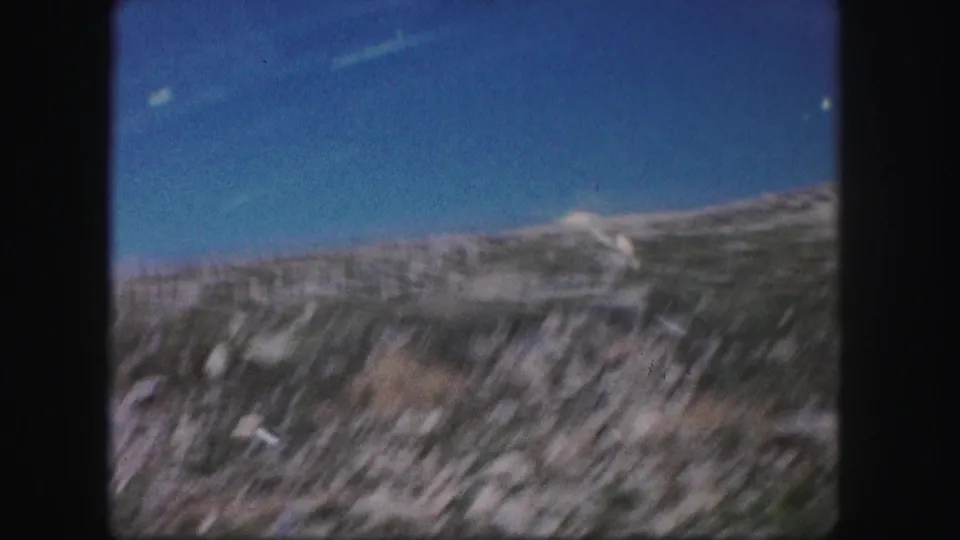 1958 Colorado frame with handheld motion blur across a stony hillside, sparse plants, and bright blue sky.
