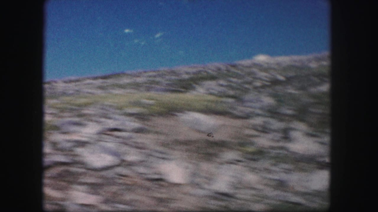 1958 Colorado 8mm frame showing a blurred rocky mountain slope beneath a clear blue sky during a handheld pan.