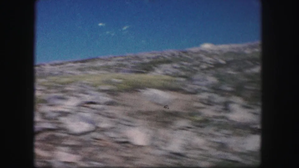 1958 Colorado 8mm frame showing a blurred rocky mountain slope beneath a clear blue sky during a handheld pan.