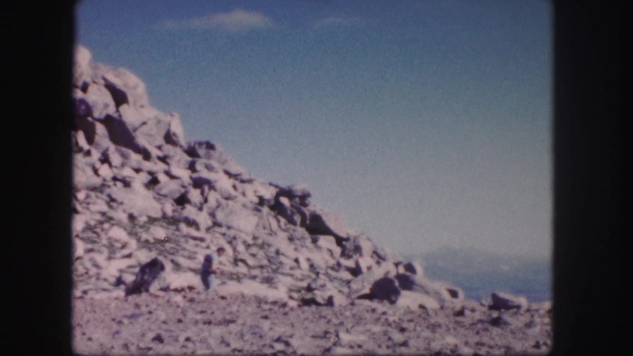 Rocky mountain outcrop with a small distant hiker under blue sky.