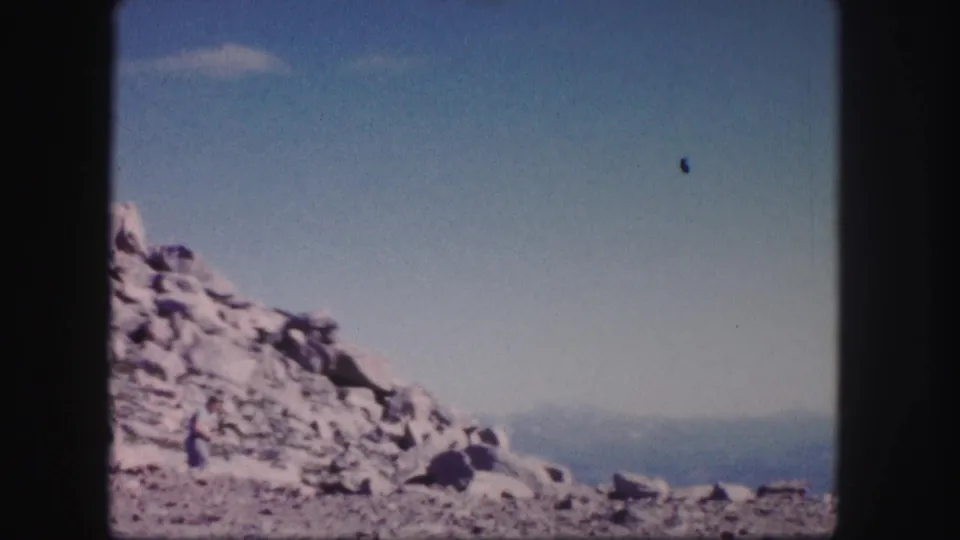 1958 Colorado 8mm frame showing a distant hiker on a pale rocky slope with hazy mountains on the horizon.