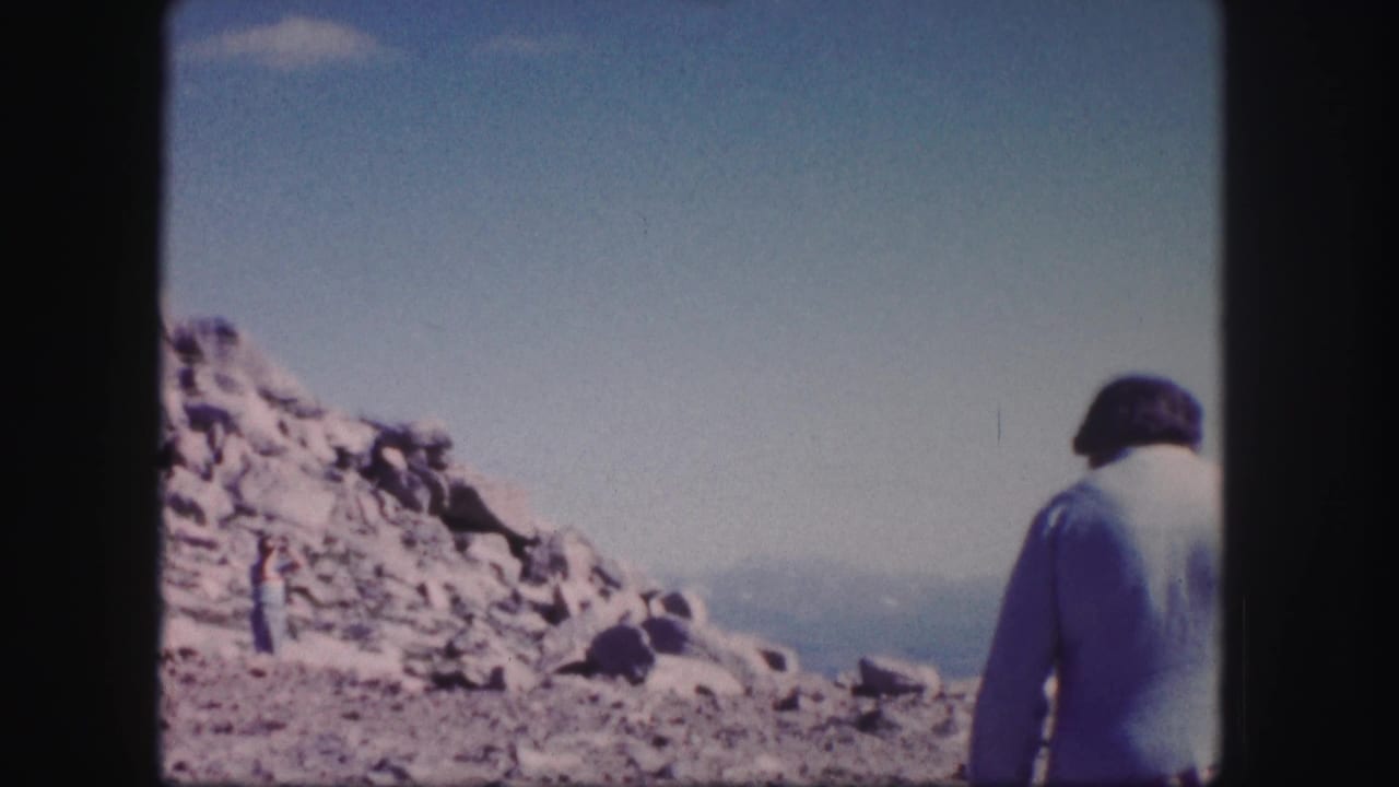 Person in a light shirt and dark cap walks near a rocky slope.
