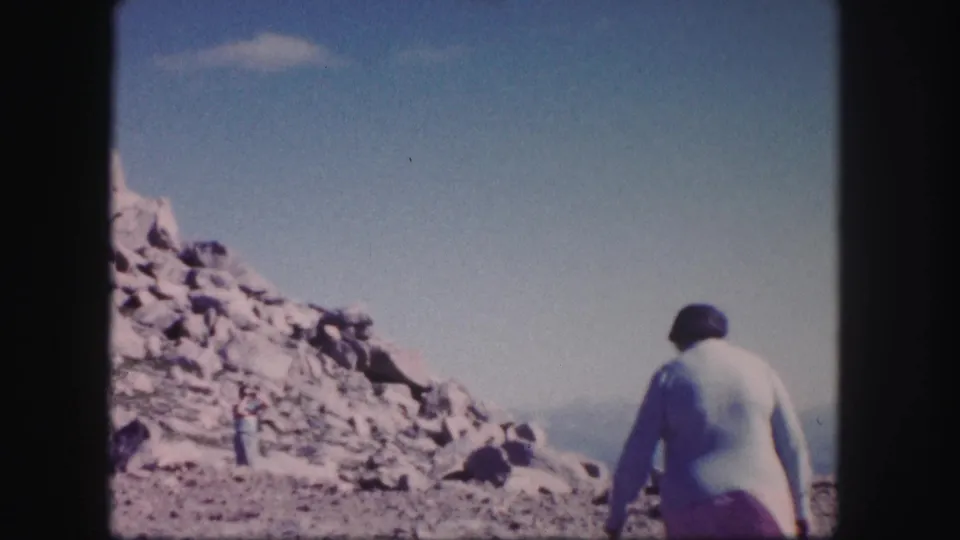1958 Colorado 8mm frame with a person walking away on a rocky slope and a second figure near the rocks.