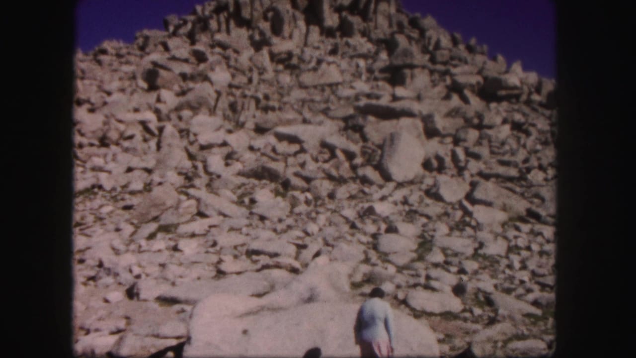 Woman at the base of a rocky slope with scattered boulders around her.