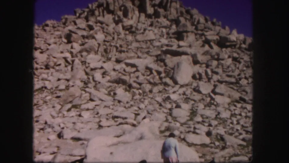 1958 Colorado 8mm frame with a woman partly visible at the lower edge of a pale boulder field and steep rock slope.