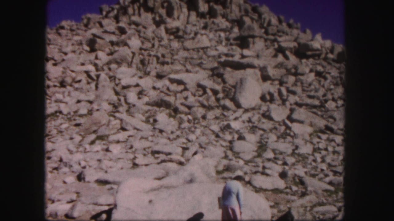 Rocky summit slope with a person partly visible near large pale boulders.