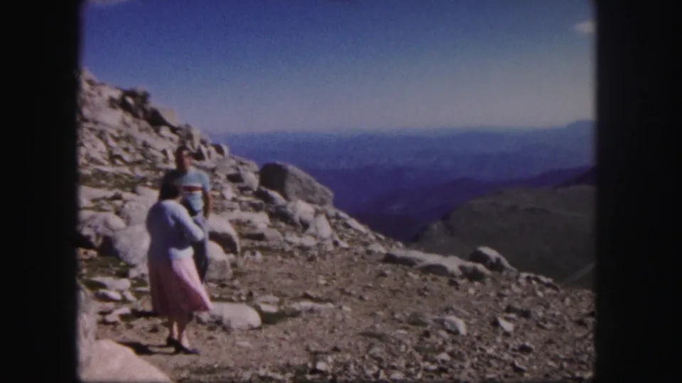1958 Colorado 8mm frame showing a woman and man on rocky high ground with hazy mountain ridges in the distance.