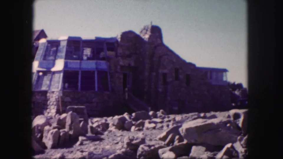A distinctive stone-and-glass building stands among summit rocks in Colorado, likely filmed during a 1958 home-movie visit.