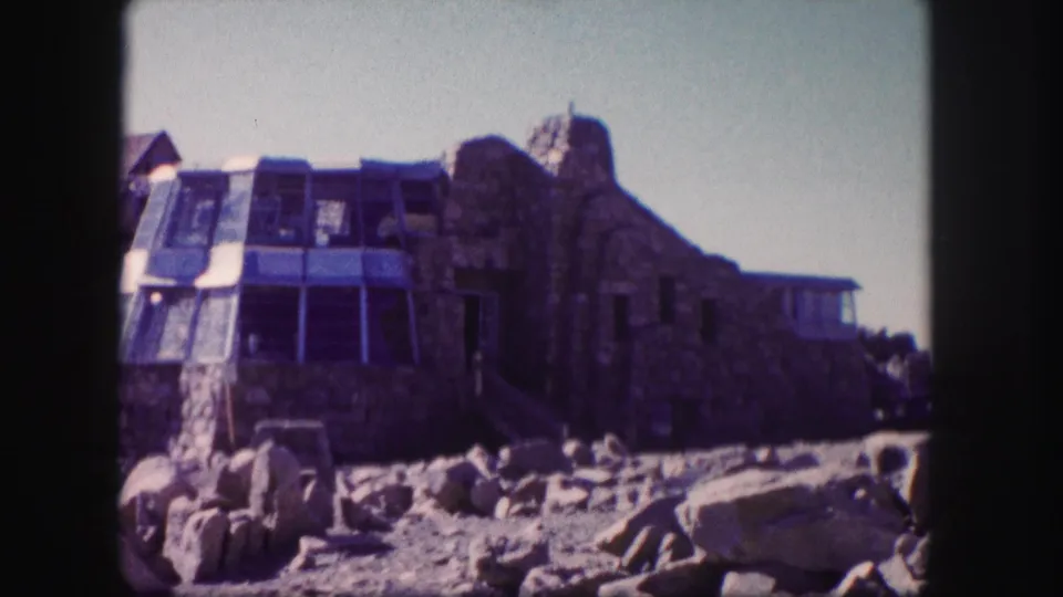 1958 Colorado 8mm frame showing a stone summit building with a glass-enclosed section and boulders in the foreground.