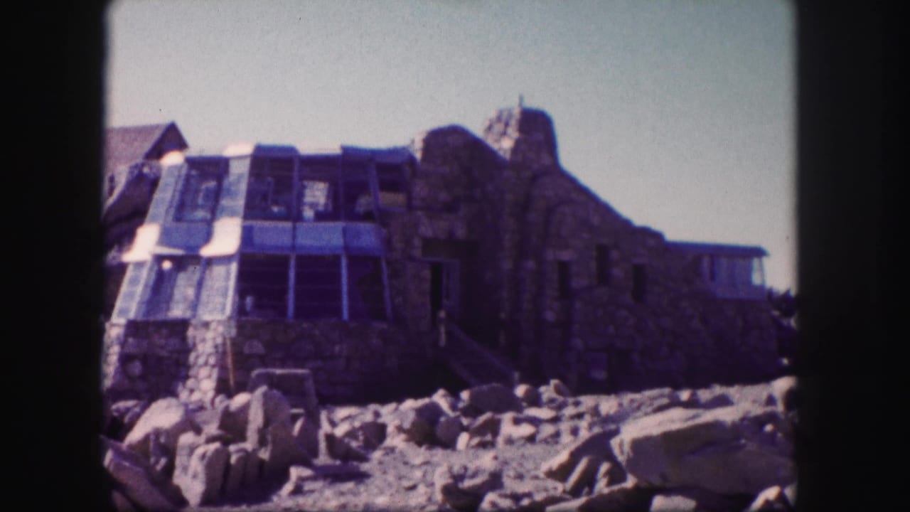 Rocky foreground leading to a stone building with glass panels.