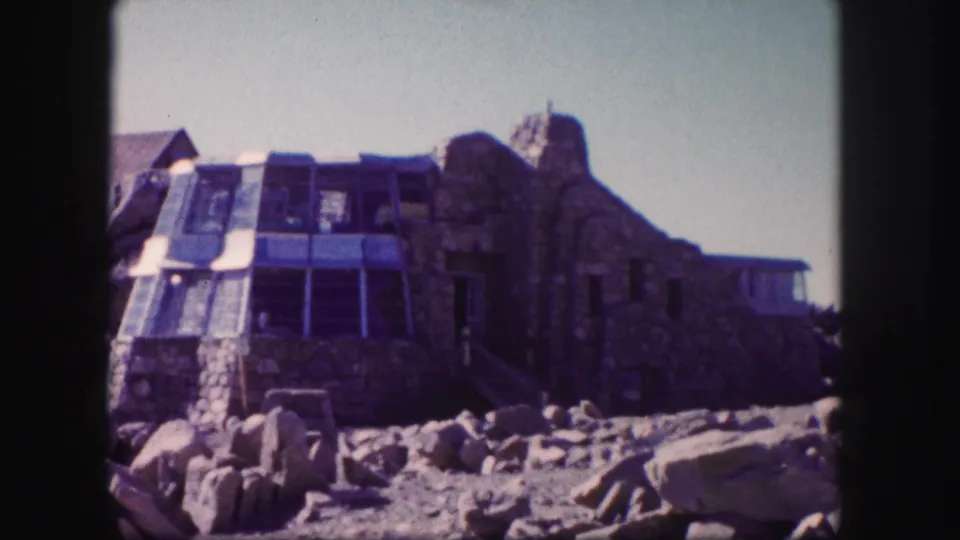 Colorado mountain exterior with a stone building, glass addition, and scattered boulders, recorded on 8mm film in 1958.