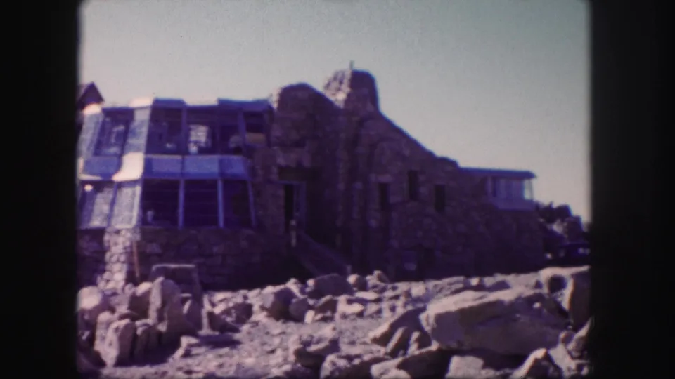 Final frame of the 1958 Colorado 8mm clip with a stone mountain building, glass enclosure, and rocky foreground.