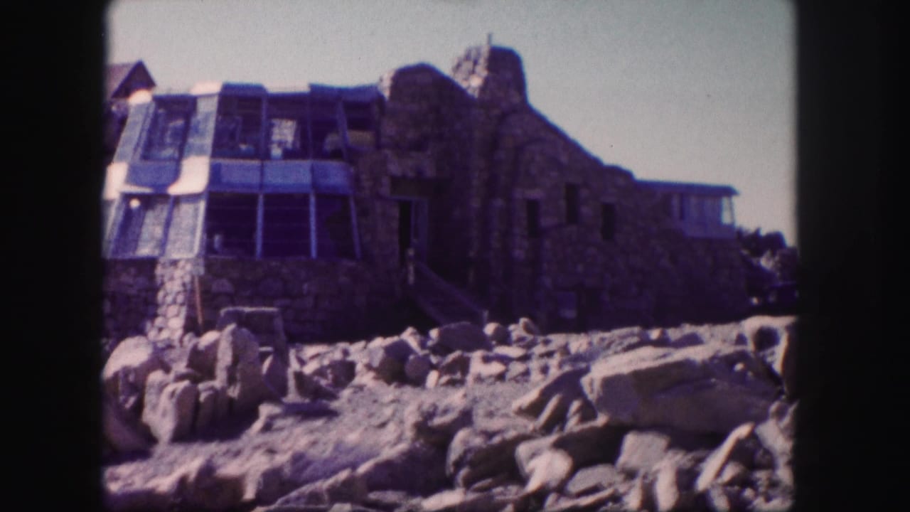 1958 Colorado 8mm frame showing a rustic stone building with glass panels and boulders in front.