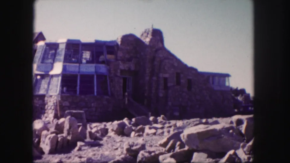 1958 Colorado home-movie view of the stone building, windowed facade, and loose rocks on a dry slope.
