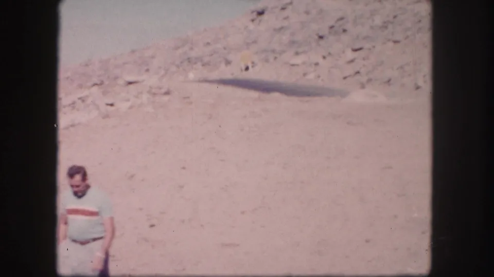 1958 Colorado 8mm frame showing a man in casual clothing on open sandy terrain below a slope.