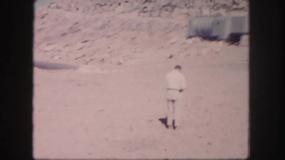 1958 Colorado home-movie frame showing a man walking across a barren sandy area with hillside behind him.