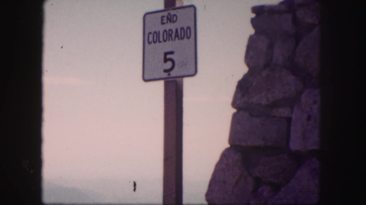 1958 Colorado 8mm frame showing an END COLORADO 5 road sign next to a rough stone pillar under a pale sky.