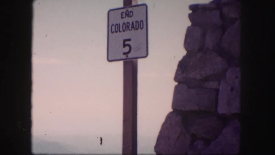 1958 Colorado 8mm frame showing an END COLORADO 5 road sign next to a rough stone pillar under a pale sky.