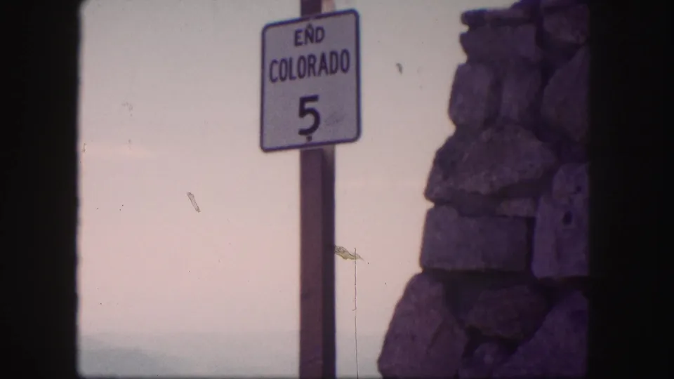 1958 home-movie frame with an END COLORADO 5 sign, rough stonework, faded color, and visible film wear.