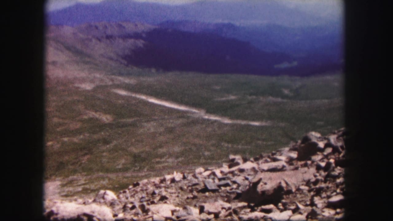 Wide mountain vista with rocks in the foreground and a winding pale path in the valley.