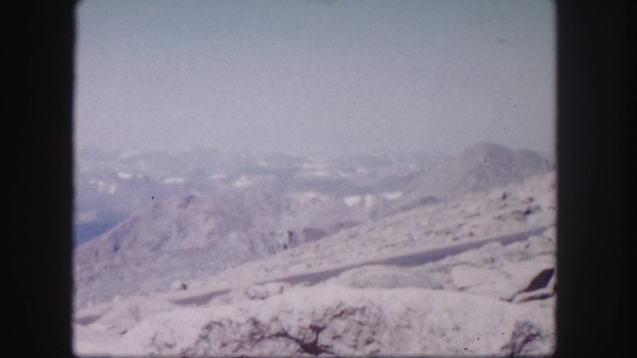 Colorado mountain landscape on 8mm film, with a snow-covered ridge in front of hazy layered peaks and a pale blue sky.