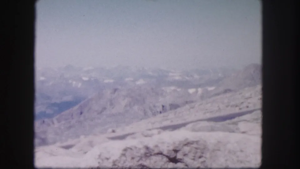 1958 Colorado landscape frame with soft-focus snowy terrain, a blue-toned valley, and distant mountain forms under bright daylight.