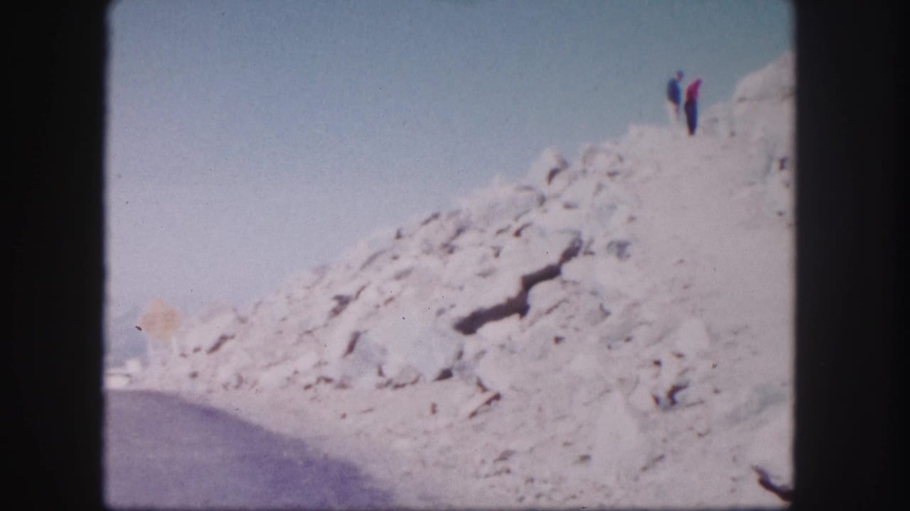 Two distant hikers stand near the top of a rocky mountain slope.