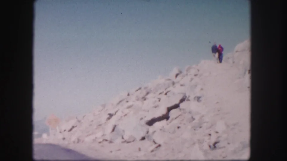 A 1958 Colorado 8mm frame shows two small hikers on a pale rocky ridge, with soft focus and faded home-movie color.