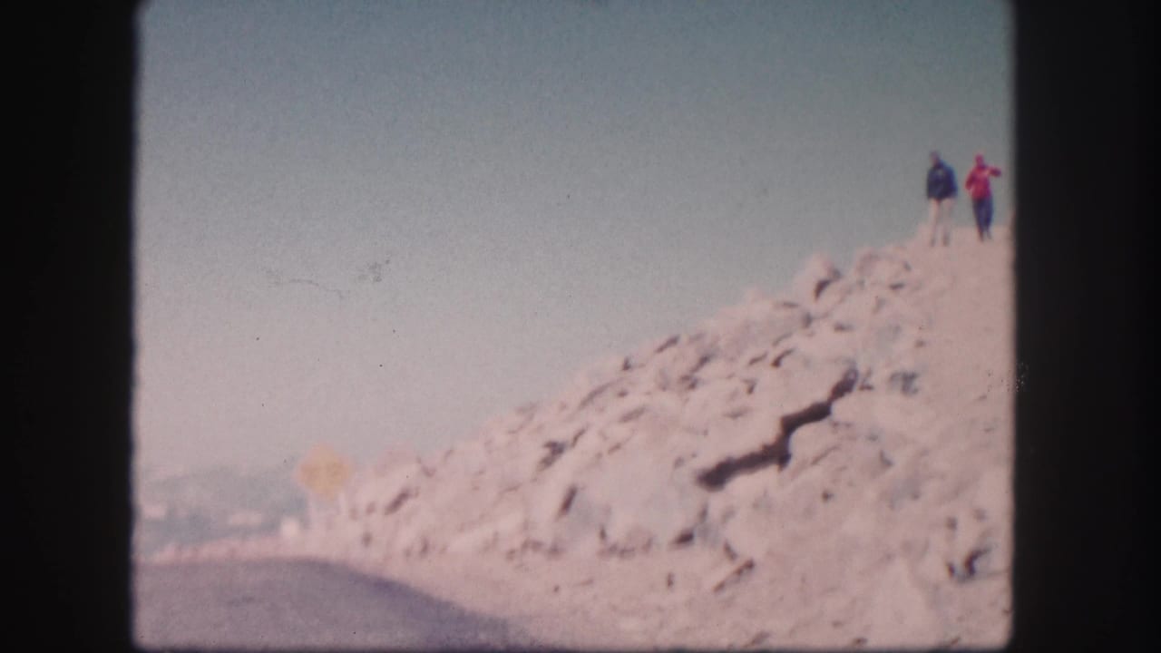 Two people appear near the crest of a rocky Colorado roadside slope, seen in soft 1958 8mm color footage.