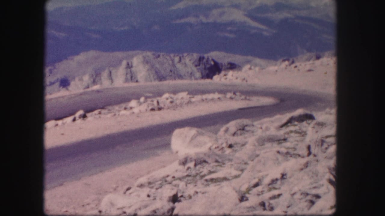 1958 Colorado 8mm frame showing a curving road through rocky mountain terrain with distant ridges and open sky.