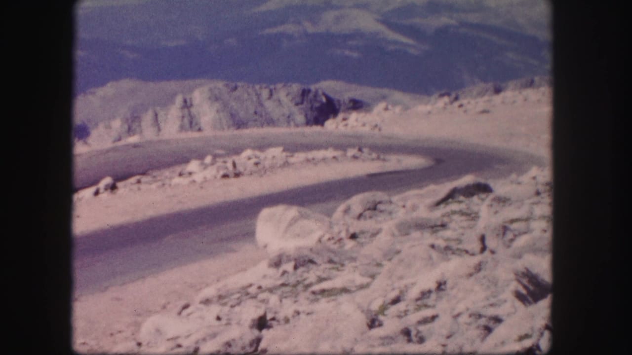 1958 Colorado 8mm frame showing an empty hairpin mountain road bordered by pale rocks and distant peaks.