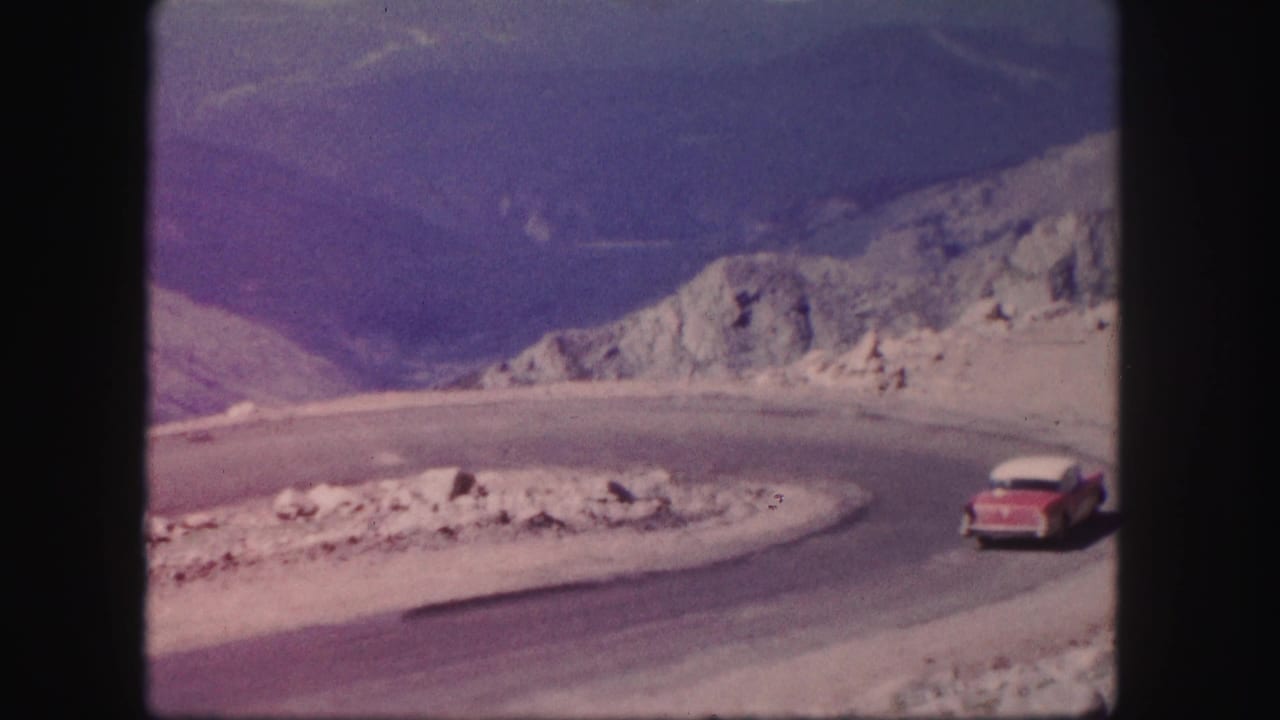 A red and white car approaches a winding Colorado mountain road curve in 1958 8mm home-movie footage.