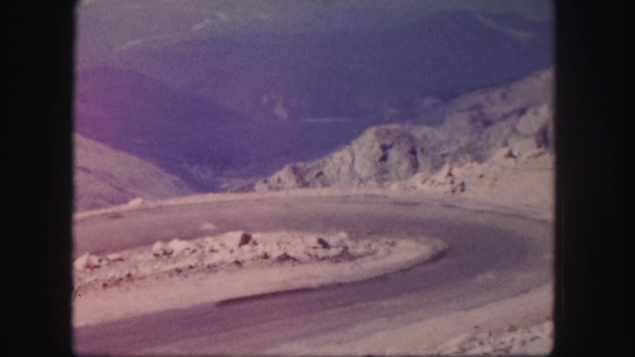 Empty curved mountain road with rocky slopes and distant peaks.