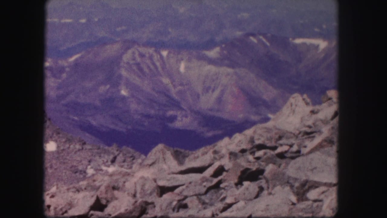 1958 Colorado 8mm frame showing gray rock formations in the foreground and layered mountain ridges fading into haze.