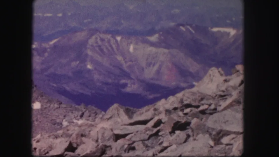 1958 Colorado 8mm frame showing gray rock formations in the foreground and layered mountain ridges fading into haze.