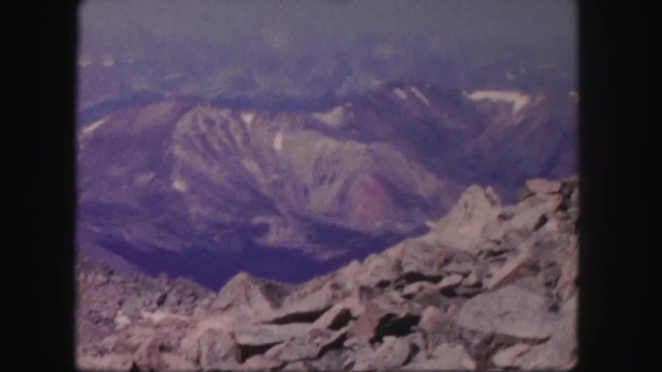 1958 Colorado home-movie frame showing jagged gray rock and a broad hazy mountain range with analog color shift.