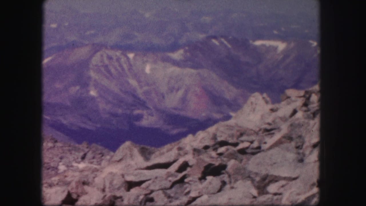 Rocky alpine foreground with distant mountain ridges under a blue sky.