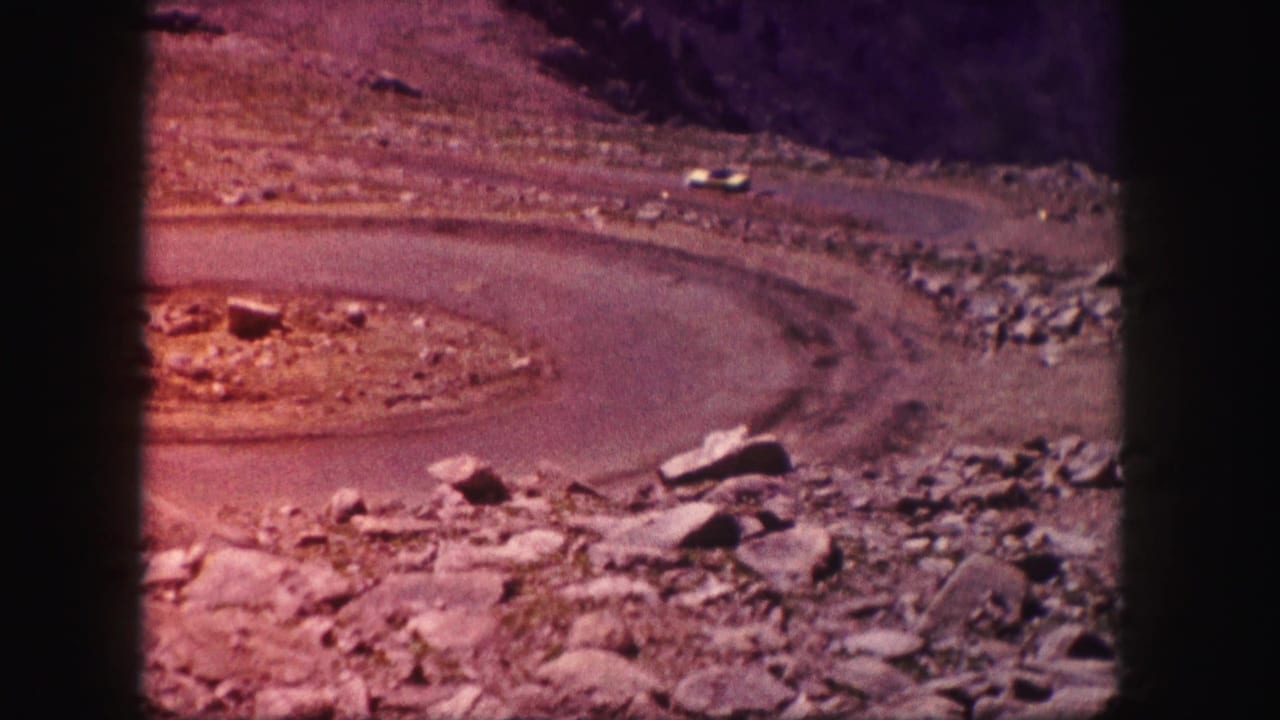 1958 Colorado 8mm frame showing a winding paved road through rocky desert ground, with stones and scrub visible around the curve.